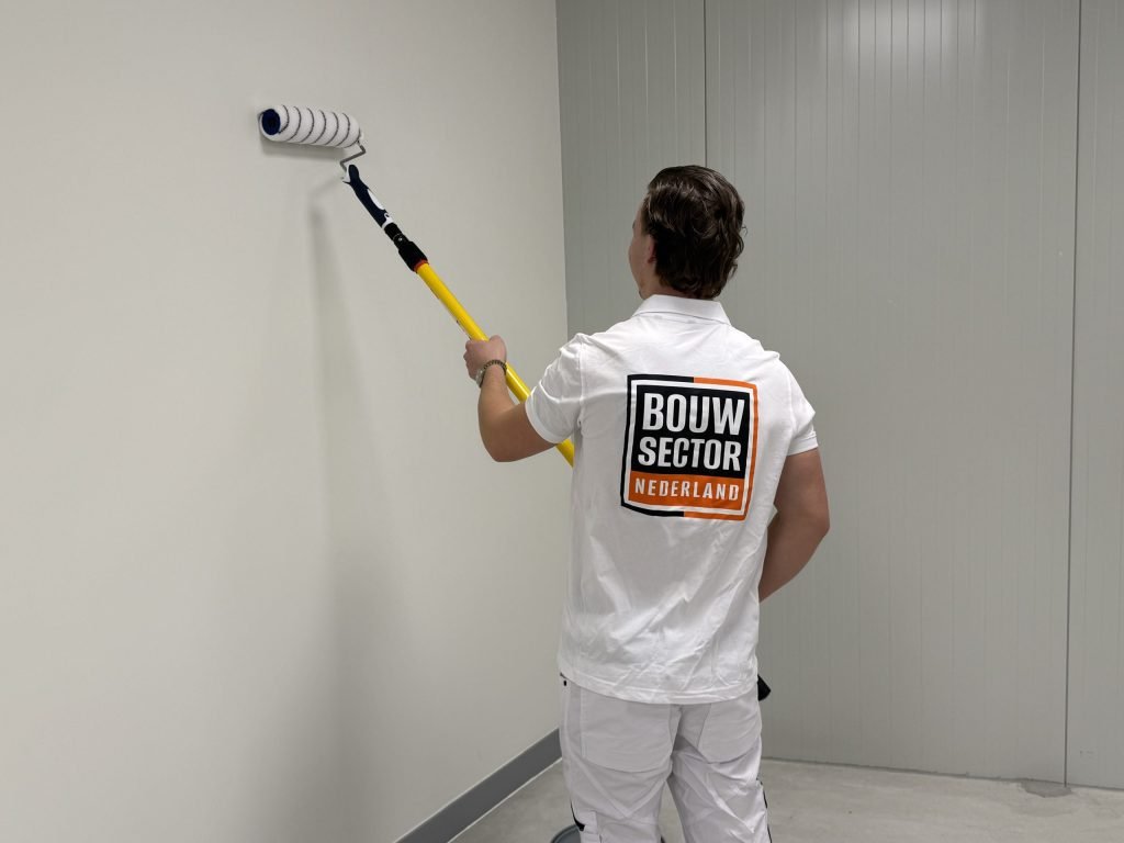 Schilder rolt de bovenkant van een kale witte wand in een lege ruimte