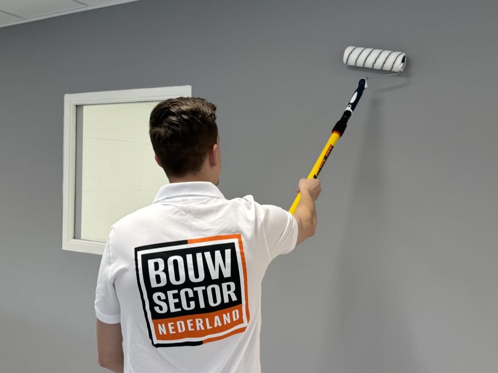 Schilder van Bouwsector Nederland rolt een grijze muur naast een raam met een verlengsteel