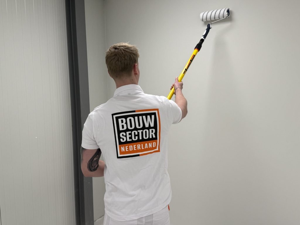 Schilder met verlengde roller werkt een lichte wand naast een deurpost af