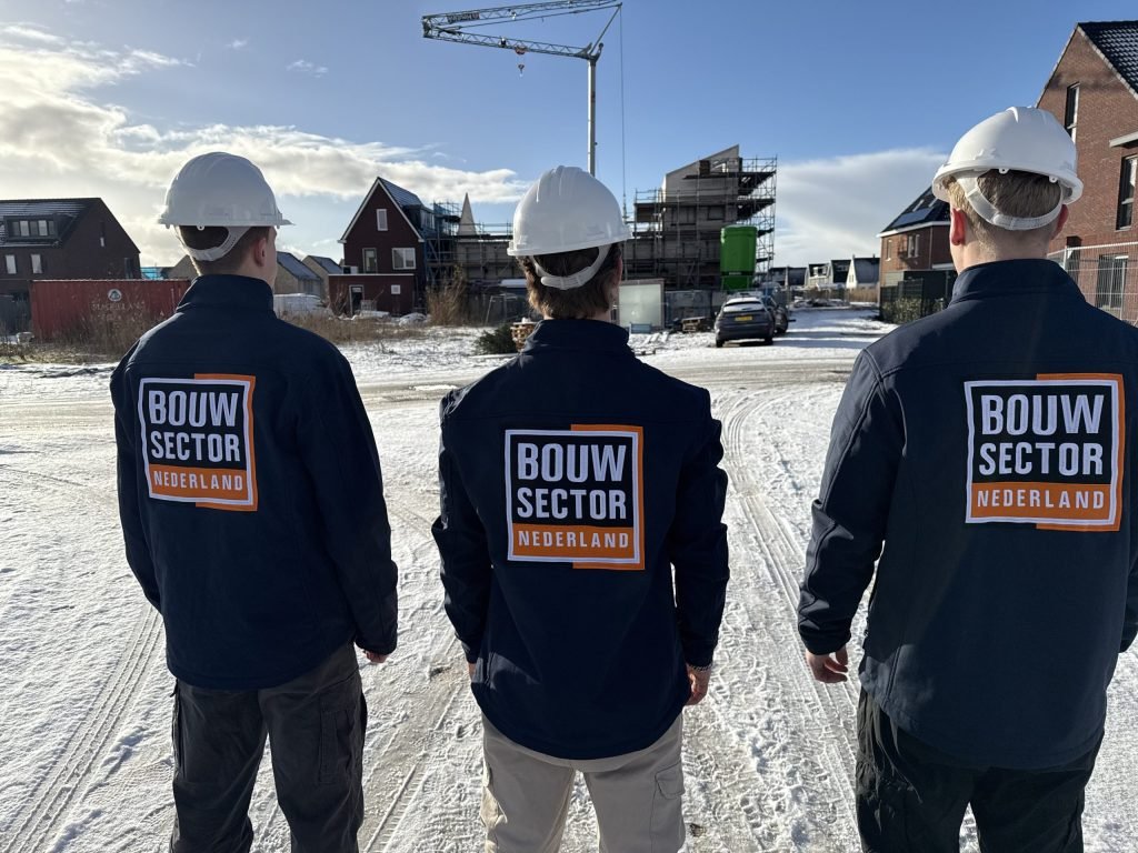 Drie medewerkers van Bouwsector Nederland met helm op de rug gezien bij nieuwbouwwoningen in aanbouw