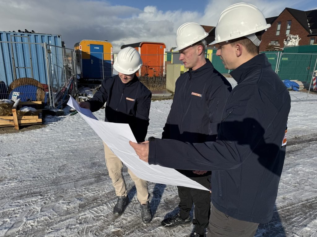 Drie medewerkers van Bouwsector Nederland met witte helm bekijken een bouwtekening op een nieuwbouwterrein
